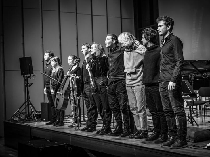Bild schwarz-weiß,  Menschen in einer Reihe auf der Bühne, sehen ins Publikum | © Fabian Schober